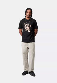 Camiseta negra con un diseño colorido y abstracto de la letra "G" en el frente, combinada con jeans gris claros y zapatos negros.