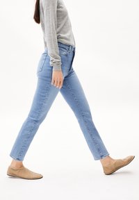 Jean bleu clair avec une coupe slim, taille mi-haute et jambes droites. Associés à des chaussures beiges à enfiler et un haut gris à manches longues.