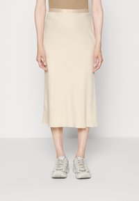 Jupe midi beige avec une texture lisse et extensible, un design sans caractéristique et une taille élastique. Associée à des chaussures de sport gris clair.