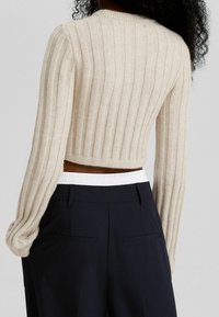 Beige ribbad stickad korttröja med långa ärmar och rundad hals. Matchad med marinblå byxor och ett vitt elastiskt midjeband.