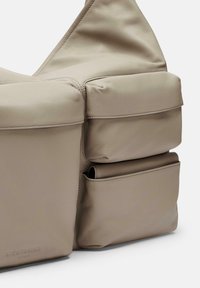 Sac en cuir beige avec un design structuré, des coutures visibles et plusieurs poches extérieures pour le rangement. Texture douce, forme moderne.