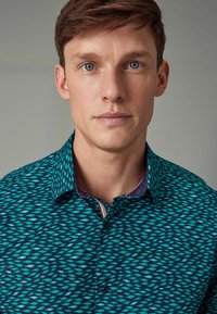 Camicia a maniche corte, turchese con un motivo di pesci, presenta un design del colletto interno a contrasto. Chiusura con bottoni e colletto standard.