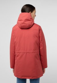 Veste imperméable rouge avec capuche, manches longues et coupe décontractée. Texture lisse et détail accentué à la taille au dos.