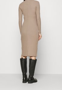 Robe côtelée à manches longues en beige tamisé, longueur genou avec une silhouette ajustée, associée à des bottes en cuir noir hauteur genou.