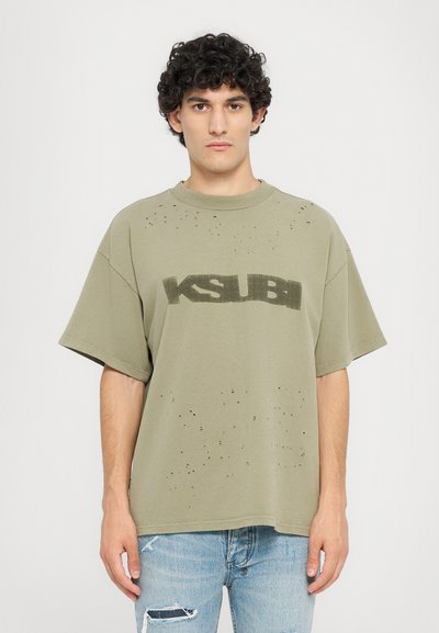 Olivegrünes, übergroßes T-Shirt aus Baumwolle mit einem abgenutzten Design, sichtbaren Löchern und einem schwarzen "KSUBI"-Logo über der Brust.