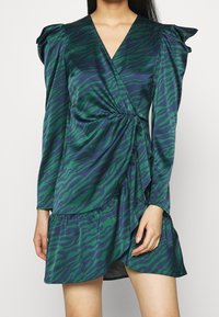 Green and navy wrap dress with tiger stripes; features long sleeves, a gathered waist, and layered ruffled hem. Made from a smooth fabric.