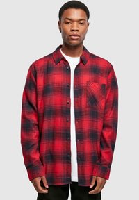 Chemise en flanelle à carreaux rouge et noir avec devant boutonné, col et une poche poitrine unique. Fabriquée en tissu texturé, elle présente des manches longues.