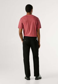 Rood katoenen T-shirt met een ontspannen pasvorm, gecombineerd met zwarte broek. De outfit heeft een eenvoudig ontwerp en een minimalistische stijl.