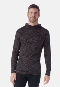 Langärmliges Kapuzenshirt mit einem dunklen geometrischen Muster in Blau, Rot und Braun. Weiches Material mit einer taillierten Passform und Daumenlöchern an den Bündchen.