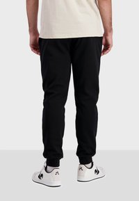 Svarta joggingsbyxor med tapered passform, tillverkade av mjukt material, med elastiska mudd och en enkel design. Matchas med vita sneakers.