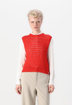 Red knitted sleeveless top with an openwork design, round neckline, and ribbed hem, layered over a white collared shirt.