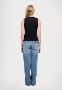 Top senza maniche di maglia nera con un motivo testurizzato, abbinato a jeans in denim blu chiaro a gamba larga con vita alta e tasche posteriori.