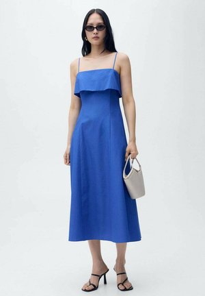 Blue midi dress with a ruffled strapless design, smooth fabric, and a loose fit. Paired with black strappy heels and a small beige handbag.
