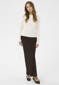 Witte blouse met lange mouwen, gecombineerd met een lange, donkerbruine rok. Het model draagt zwarte flats. Eenvoudige, klassieke ontwerpen met zachte texturen.