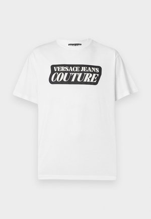 Biała koszulka z krótkim rękawem z czarnym prostokątnym logo z napisem "VERSACE JEANS COUTURE" na środku klatki piersiowej.