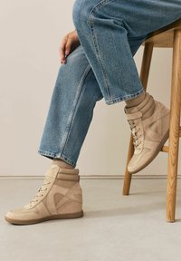 Beige korkeavartiset tennarit, joissa on sileä nubukki päällinen ja pehmustettu kainalo, varustettuna nauhakiinnityksellä ja kontrastivärisillä yksityiskohdilla.
