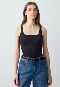 Body nero con spalline larghe e scollatura quadrata, abbinato a jeans in denim blu a vita alta e una cintura nera.