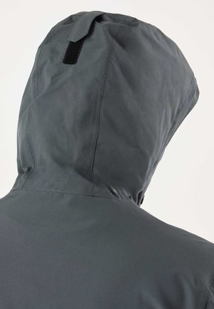 Nærbillede af bagsiden af en mørkegrå hættetrøje med synlige syninger og en sort rektangulær klap på hætten.