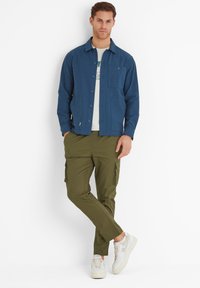 Blue button-up jacket with two chest pockets, paired with olive green cargo pants and white sneakers featuring light accents.