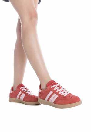 Zapatillas de ante rojas con rayas y cordones blancos, con una puntera redondeada y suela de goma marrón. La marca es visible en la lengüeta.