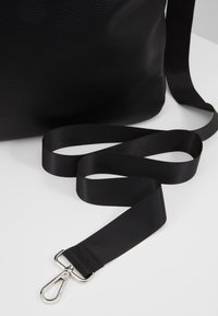 Černá kožená kabelka s texturovaným povrchem, vybavená černým popruhem a kovovým klipem, ukazující hladkou tkaninu a čisté okraje.