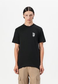 Sort bomulds t-shirt med et lille hvidt logo på venstre bryst. Korte ærmer og rund hals med en lige pasform og minimalistisk design.