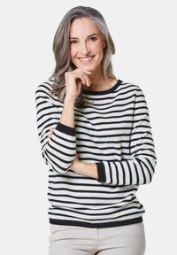 Gestreifter Pullover in Schwarz und Weiß, Rundhals, lange Ärmel mit schwarzen Bündchen, weicher Stoff, getragen mit hellen Hosen.