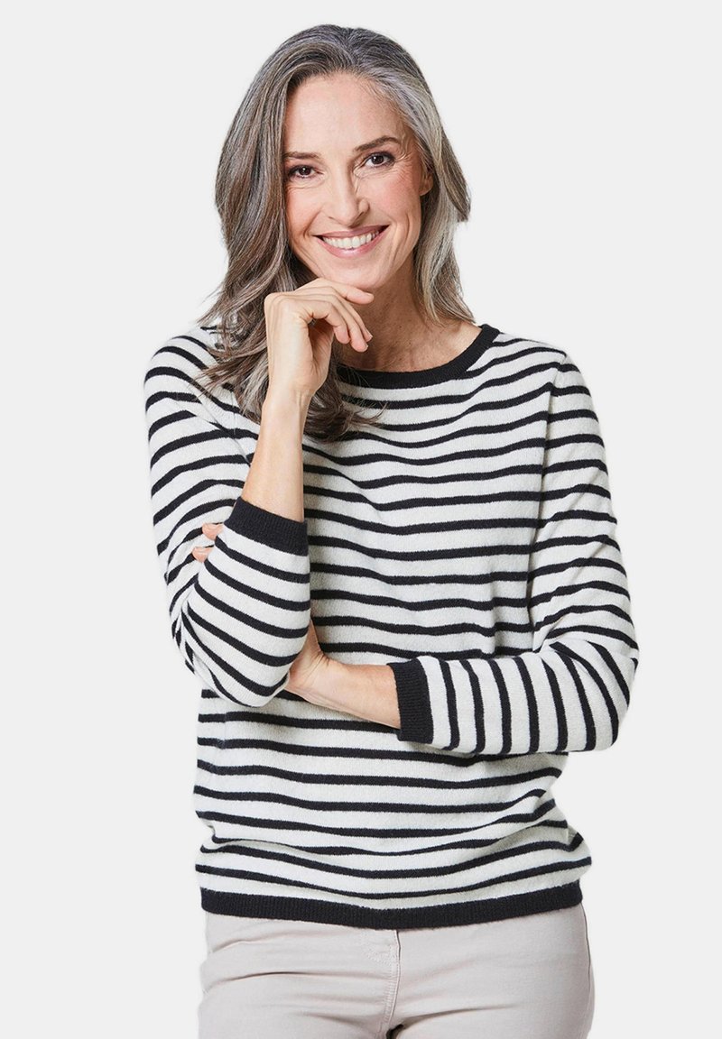 Gestreifter Pullover in Schwarz und Weiß, Rundhals, lange Ärmel mit schwarzen Bündchen, weicher Stoff, getragen mit hellen Hosen.