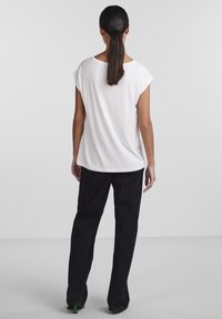 Vit kortärmad topp med avslappnad passform, kombinerad med svarta vida byxor och skorna med gröna accenter. Slät tyg och avslappnad design.