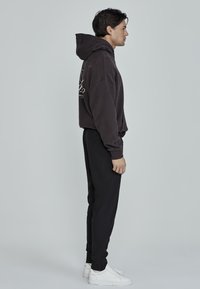 Hanorac gri închis, cu o croială lejeră, buzunar frontal tip kangaroo și detalii ale logo-ului alb. Asortat cu pantaloni jogger negri, tapered și adidași albi.