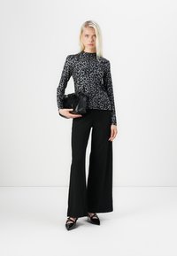 Long-sleeve, form-fitting top with a black and gray leopard print, paired with wide-leg black trousers and a textured black handbag.