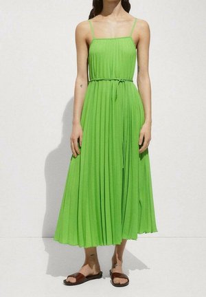 Mujer con un vestido midi sin mangas plisado de color verde lima y un cinturón delgado, combinado con sandalias planas marrones.