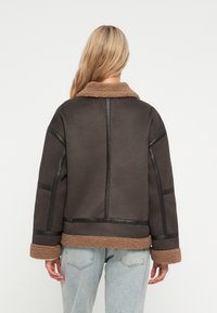 Smešni smeđi kaput od ovčje kože s crnim kožnim detaljima, oversized dizajn i krzneni ovratnik; ima teksturiranu tkaninu i vidljive šavove.
