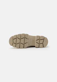Suela de goma beige claro con tacos profundos y una textura estriada, diseñada para ofrecer tracción y durabilidad. Marcada con un logo y detalles de tamaño.