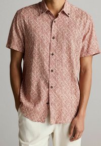 Chemise à manches courtes en bordeaux avec un motif en losanges. Fabriquée en tissu léger, elle comporte des boutons noirs et une coupe décontractée.