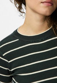 Tumši zaļa ribota džemperis ar horizontālām baltām svītrām un aploka kaklu, izceļot teksturētu audumu.
