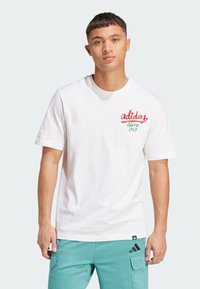 Hvid bomuld T-shirt med rødt og grønt broderet "adidas" logo og "since 1949" tekst på venstre bryst. Korte ærmer, rund hals.