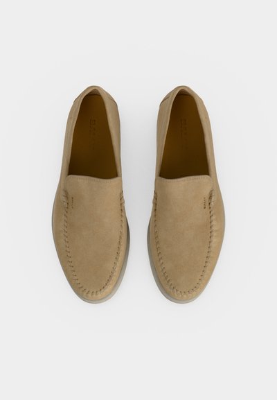 Ζευγάρι μπεζ αντικέ γόβες τύπου slip-on με ορατή ραφή γύρω από το δάχτυλο και μαλακές λεπτομέρειες από καουτσούκ, προβολή από πάνω σε λευκό φόντο.