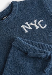 Ensemble en tricot bleu doux composé d'un pull et d'un pantalon, avec l'inscription blanche "NYC" sur la poitrine, et des poignets et une taille côtelés.