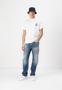 Hvit bomulls t-skjorte med en liten fargerik trykk på venstre bryst, kombinert med falmet blå jeans med slitte detaljer og hvite sneakers.