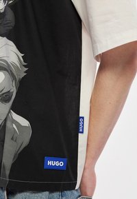 Μαύρο και άσπρο γραφικό μπλο υζάκι με αντίθετο άσπρο πάνελ. Διαθέτει εκτύπωση χαρακτήρα και δύο μπλε ετικέτες "HUGO" στο τελείωμα.