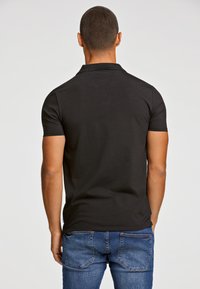Svart kortärmad polo med klassisk krage, slät textur och figursydd design, i kombination med blå denimjeans.