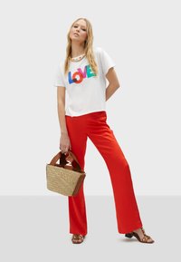 Bílá tričko s barevným potiskem "LOVE", spárované s červenými širokými kalhotami. Tkaná kabelka a hnědé sandály na vysokém podpatku se zlatými akcenty.