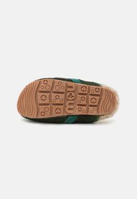 Mou slipper featuring a green fur upper, beige fur lining, and a sturdy orange rubber sole with textured grip patterns.