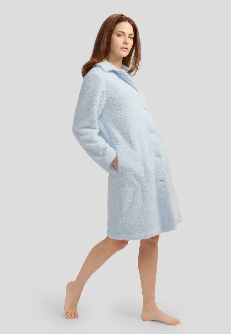 Bata de baño de color azul claro, esponjosa, de longitud hasta la rodilla, con frente abotonado, cuello con muesca y dos bolsillos laterales, con una tela texturizada.