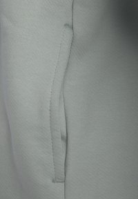 Tejido de sudadera azul claro con una textura suave, que presenta un bolsillo lateral y detalles de costura visibles. Vista en primer plano del material.