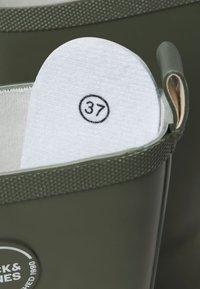 Zielony gumowy but z białą wyjmowaną wkładką oznaczoną rozmiarem buta 37 wewnątrz buta.