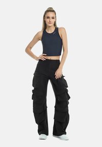Sininen crop top valmistettu sileästä kankaasta, yhdistettynä mustiin cargo-housuihin, joissa on kerrokselliset taskut ja leveät lahkeet. Valkoiset tennarit täydentävät asun.