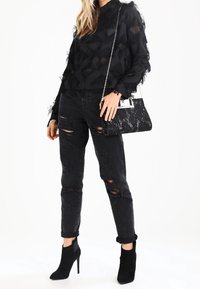 Musta läpikuultava paita kolmiomaisilla kuvioilla, yhdistettynä kulutettuihin mustiin farkkuihin. Asusteita ovat teksturoitu musta käsilaukku ja mustat korkeakorkoiset saappaat.