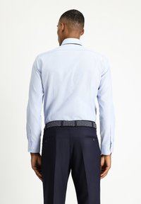 Camicia azzurro chiaro con finitura testurizzata, dotata di colletto a spread e polsini con bottone, abbinata a pantaloni scuri su misura e una cintura intrecciata.